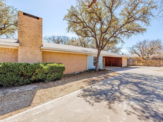 view of home's exterior featuring concrete driveway, fence, brick siding, and a chimney