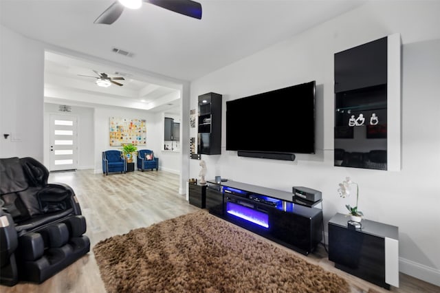 living area with visible vents, a raised ceiling, wood finished floors, and a ceiling fan