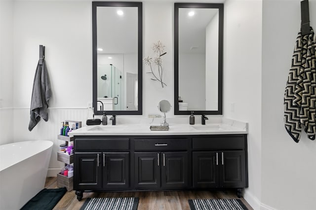 full bath featuring double vanity, a freestanding tub, wood finished floors, and a sink