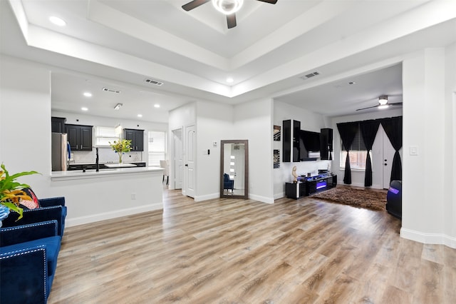 living area with a tray ceiling, visible vents, light wood-style floors, and a ceiling fan