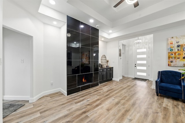 foyer with baseboards, a tray ceiling, recessed lighting, ceiling fan with notable chandelier, and light wood-type flooring