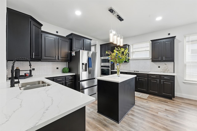 kitchen with a sink, appliances with stainless steel finishes, light wood-style flooring, and pendant lighting