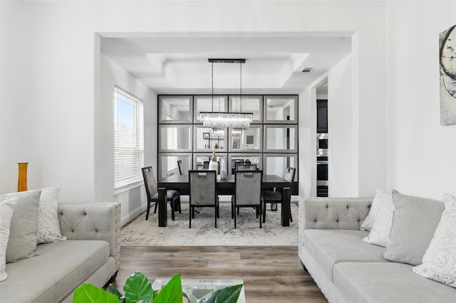 living area with a tray ceiling, wood finished floors, visible vents, and a chandelier