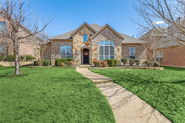 french provincial home featuring brick siding, stone siding, a shingled roof, and a front yard