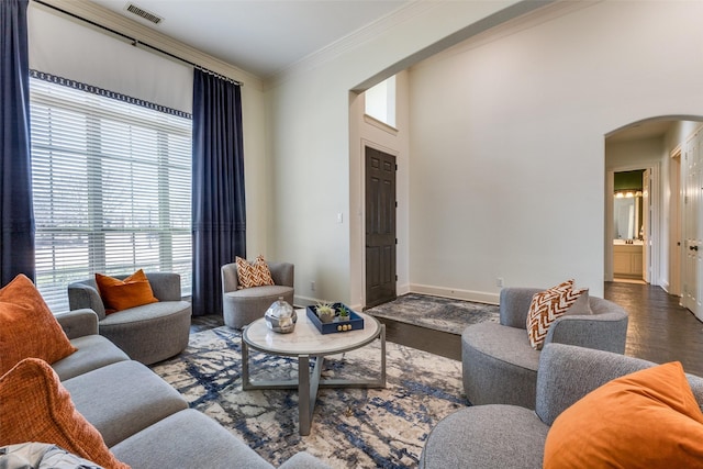 living area with arched walkways, visible vents, crown molding, and baseboards