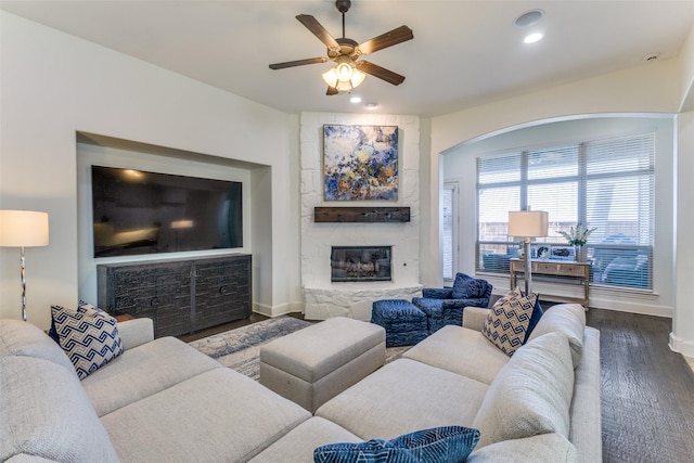 living room featuring wood finished floors, a ceiling fan, recessed lighting, arched walkways, and a stone fireplace