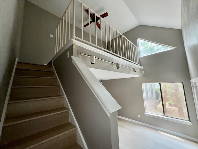 stairway featuring high vaulted ceiling, baseboards, a ceiling fan, and wood finished floors