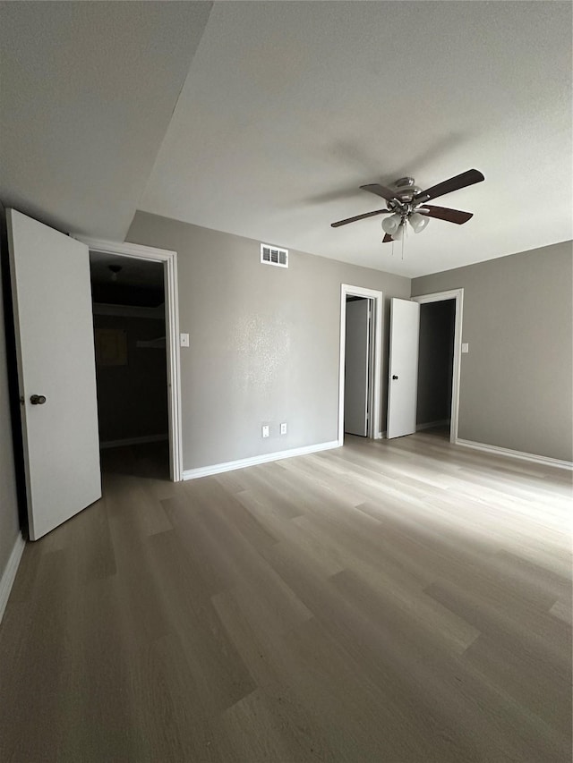 unfurnished room with a ceiling fan, wood finished floors, visible vents, and baseboards