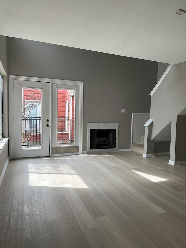 unfurnished living room featuring a premium fireplace, baseboards, wood finished floors, and stairs