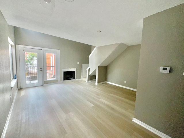 unfurnished living room featuring stairs, light wood-style flooring, baseboards, and a high end fireplace