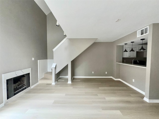 unfurnished living room featuring visible vents, a sink, wood finished floors, a high end fireplace, and baseboards