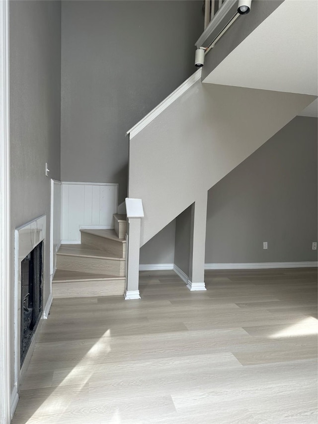 unfurnished living room with a fireplace, stairs, baseboards, and wood finished floors