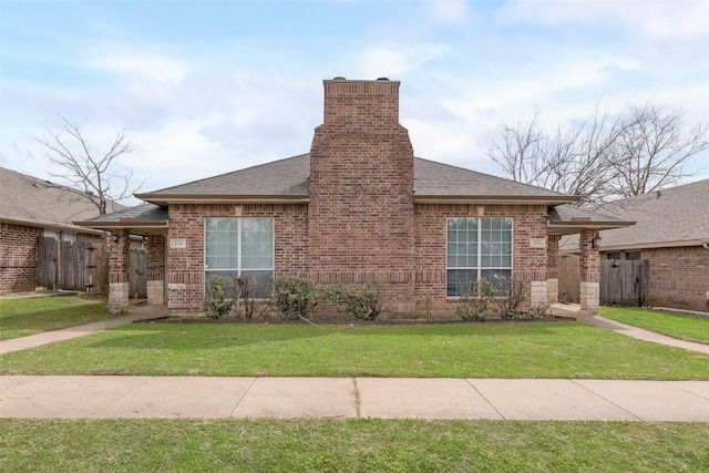 view of front of home with a front lawn, fence, brick siding, and roof with shingles