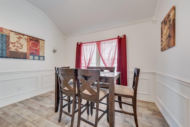 dining area with lofted ceiling, light wood-style floors, ornamental molding, and wainscoting