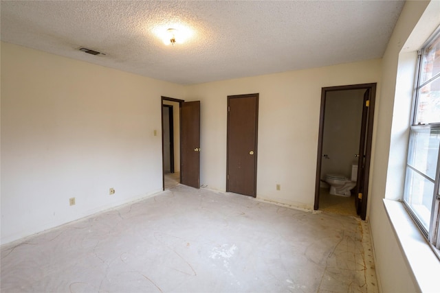 unfurnished bedroom featuring connected bathroom, visible vents, and a textured ceiling