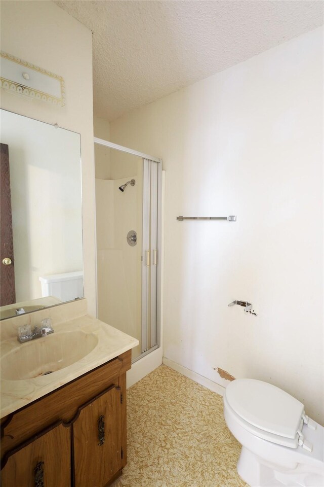 full bathroom featuring a shower stall, baseboards, toilet, vanity, and a textured ceiling