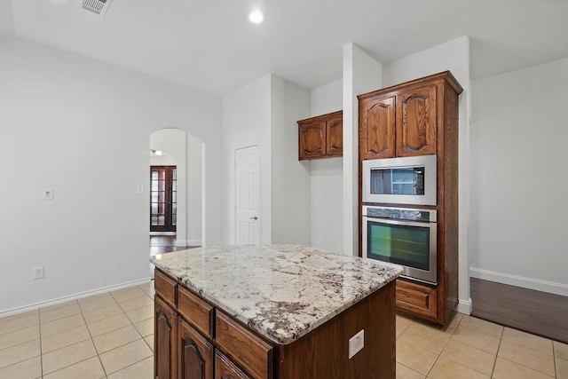 kitchen with a kitchen island, light stone countertops, light tile patterned floors, appliances with stainless steel finishes, and arched walkways