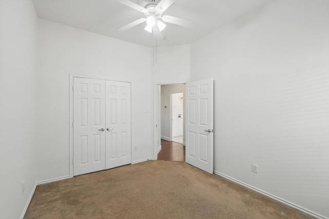 unfurnished bedroom featuring ceiling fan, baseboards, carpet floors, a high ceiling, and a closet