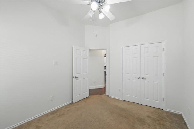 unfurnished bedroom featuring a ceiling fan, a closet, carpet, a high ceiling, and baseboards