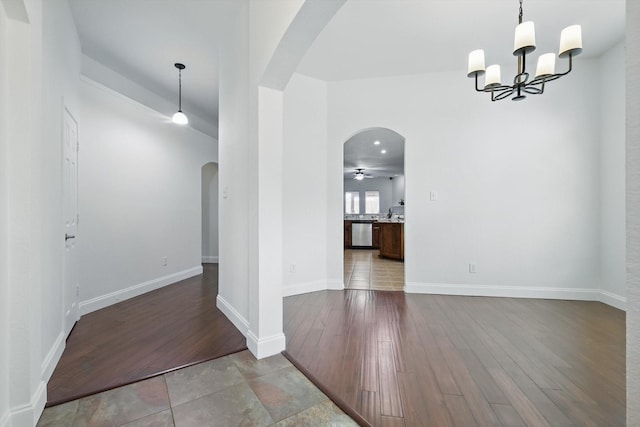 unfurnished dining area featuring baseboards, wood finished floors, arched walkways, and a chandelier