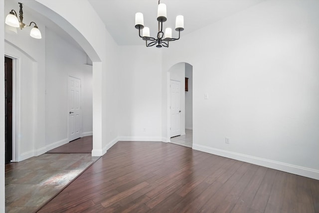 unfurnished dining area featuring baseboards, arched walkways, a notable chandelier, and wood finished floors