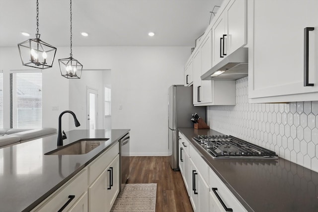 kitchen with a notable chandelier, under cabinet range hood, a sink, dark countertops, and decorative backsplash