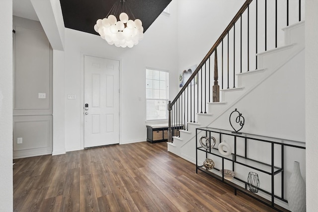 foyer with stairway, wood finished floors, baseboards, a high ceiling, and a chandelier