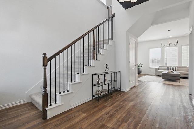 stairway featuring baseboards, a notable chandelier, a high ceiling, and wood finished floors