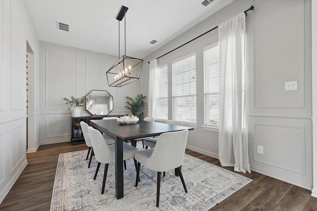 dining area with visible vents, a notable chandelier, dark wood-style flooring, and a decorative wall