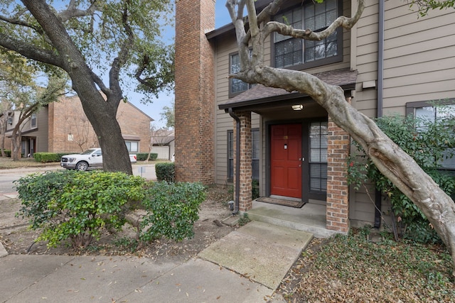 view of exterior entry with brick siding and a chimney