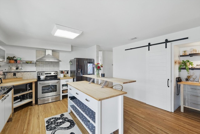 kitchen featuring open shelves, stainless steel appliances, wood counters, a barn door, and wall chimney range hood