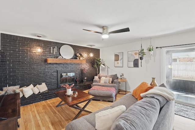 living room featuring a brick fireplace, brick wall, baseboards, ceiling fan, and wood finished floors