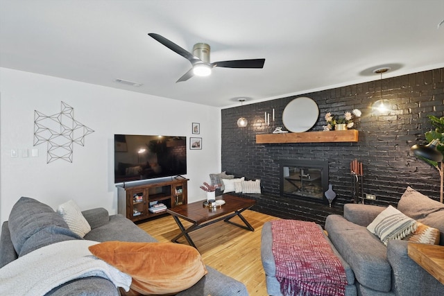 living area with visible vents, brick wall, a fireplace, wood finished floors, and a ceiling fan