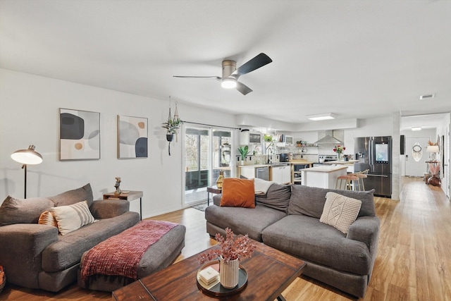 living area featuring light wood-style flooring, baseboards, and ceiling fan