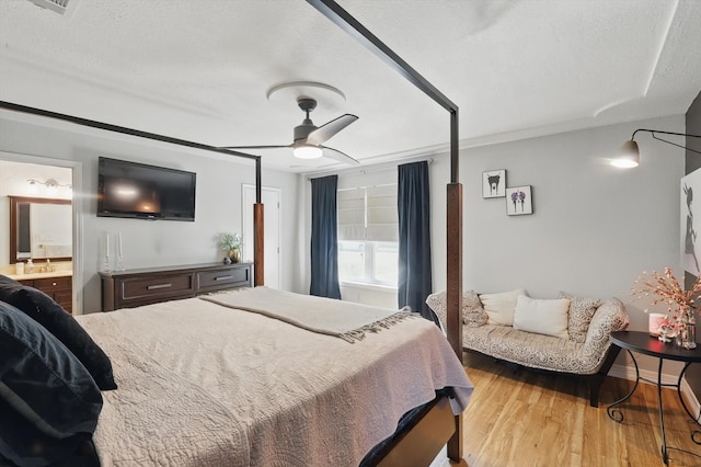 bedroom featuring a ceiling fan, wood finished floors, baseboards, ensuite bath, and a textured ceiling