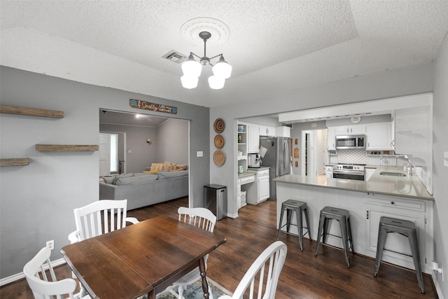 dining room with dark wood-style floors, visible vents, baseboards, a textured ceiling, and a notable chandelier