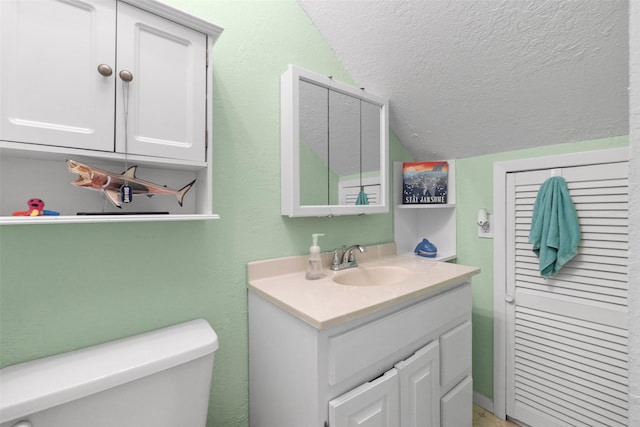 bathroom with lofted ceiling, a textured ceiling, vanity, and toilet