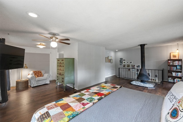 bedroom featuring ceiling fan, a textured ceiling, wood finished floors, and a wood stove