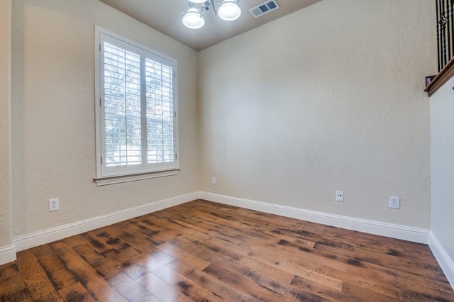 unfurnished room featuring visible vents, an inviting chandelier, baseboards, and wood finished floors