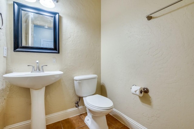 half bath featuring tile patterned flooring, toilet, a textured wall, and baseboards