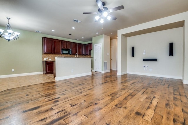 unfurnished living room featuring light wood-type flooring, visible vents, baseboards, and ceiling fan with notable chandelier