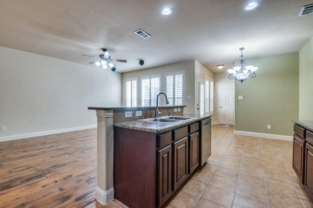 kitchen with a center island with sink, baseboards, visible vents, a sink, and ceiling fan with notable chandelier