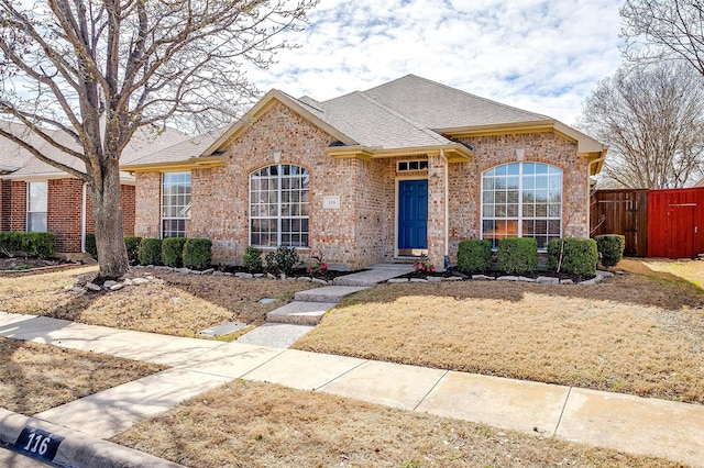 ranch-style home with fence, brick siding, and a shingled roof