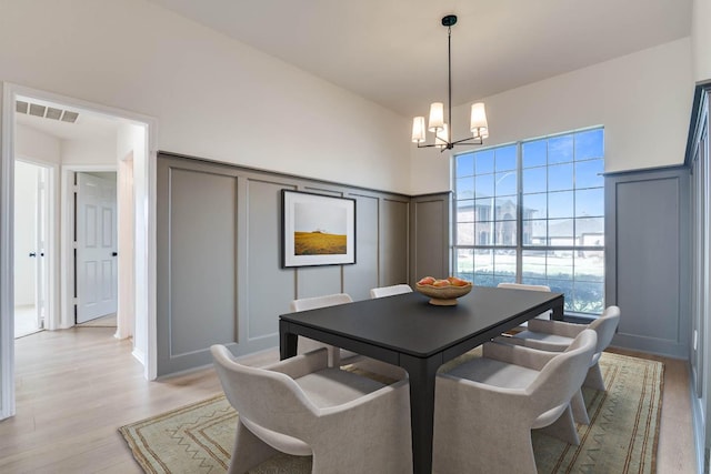 dining area with a notable chandelier, a decorative wall, light wood-style flooring, and visible vents