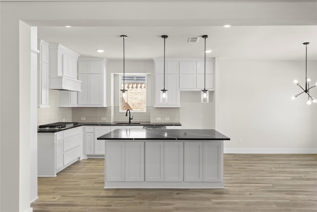 kitchen with dark countertops, visible vents, light wood-style floors, stainless steel gas stovetop, and a sink