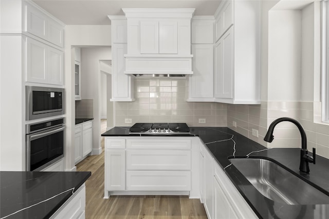 kitchen featuring light wood-type flooring, decorative backsplash, white cabinets, stainless steel appliances, and a sink