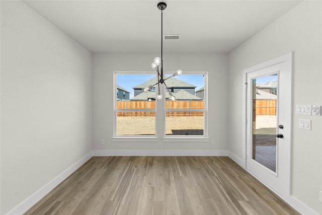 unfurnished dining area featuring wood finished floors, visible vents, a chandelier, and baseboards