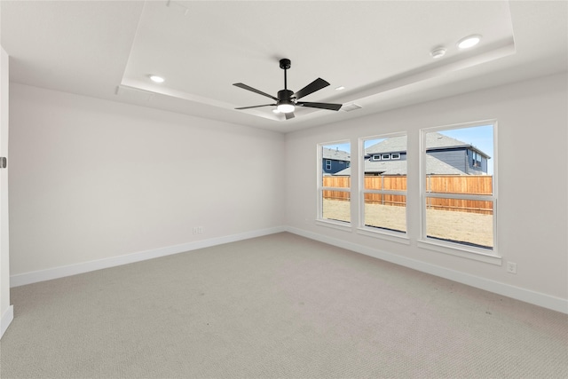 empty room with a tray ceiling, a ceiling fan, baseboards, and light carpet