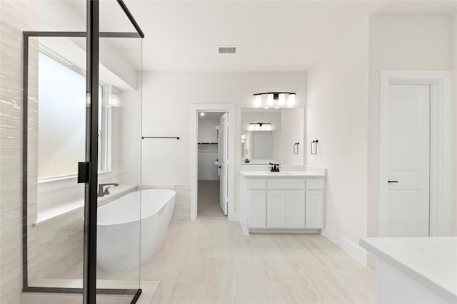 bathroom featuring visible vents, a walk in closet, a stall shower, a freestanding tub, and vanity