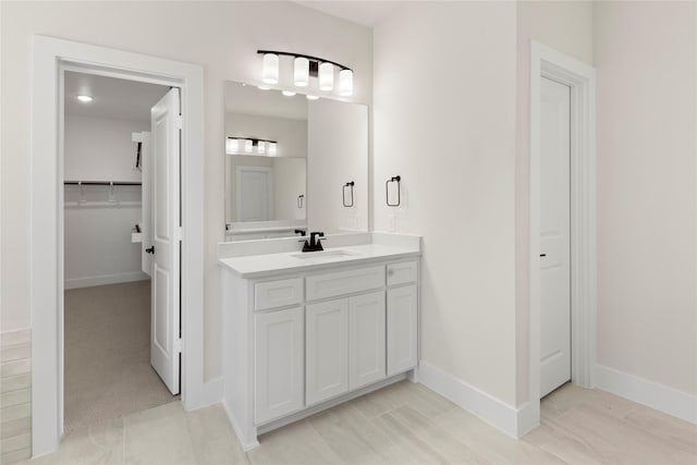 bathroom with vanity, a walk in closet, and baseboards